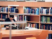 Ein Wissenschaftler mit Laptop und Buch in der Bibliothek. Foto: Mike Wolff